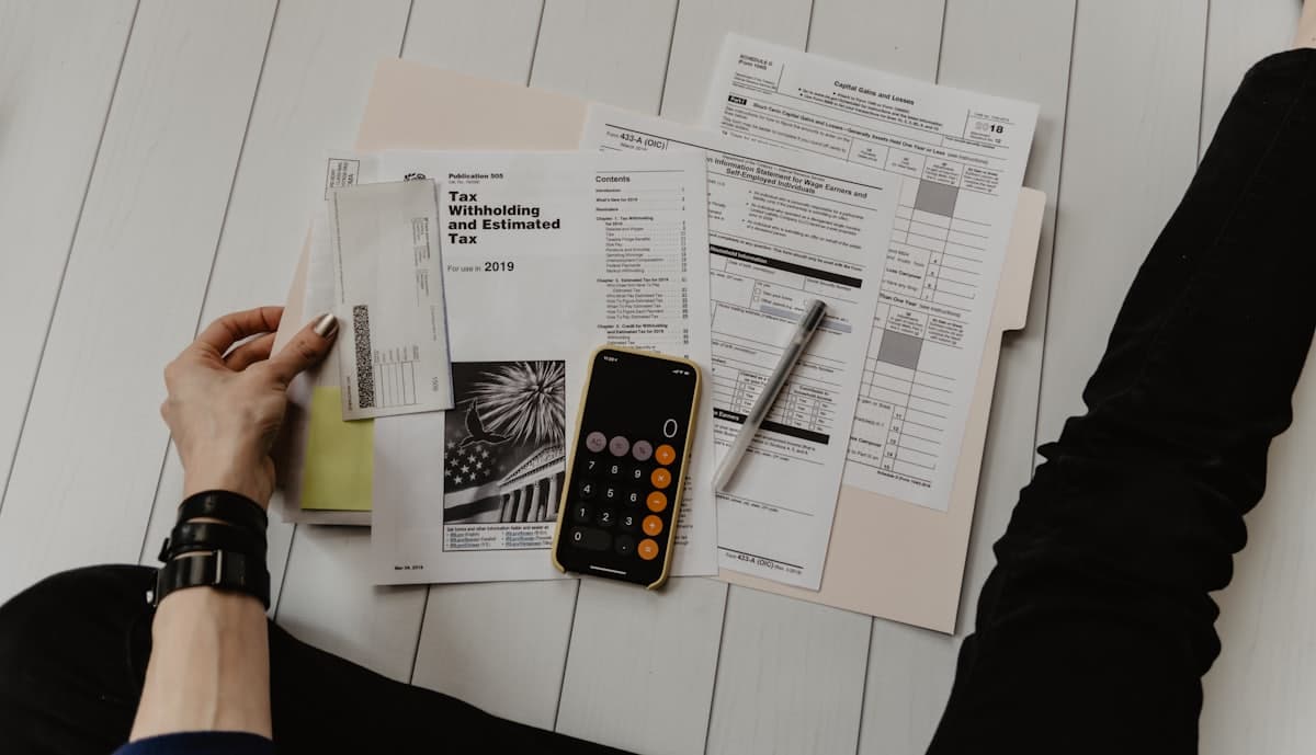 Tax forms, a calculator and a pen laid out on a desk